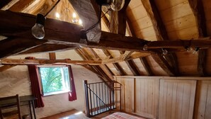 Une chambre confortable située sous les toits, avec un grand lit, des poutres apparentes, une fenêtre donnant sur un beau paysage et un petit escalier.