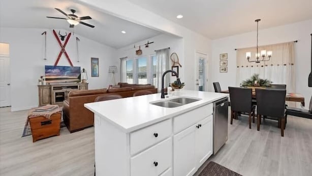 A modern kitchen with a central island, white cabinetry, and a dining area with a table and chairs. - Twin Falls National Parks Gateway (Twin Falls)