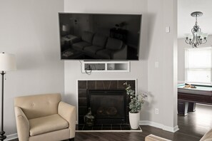 Un salon avec un téléviseur à écran plat fixé au-dessus d’une cheminée, un canapé beige et un lampadaire.