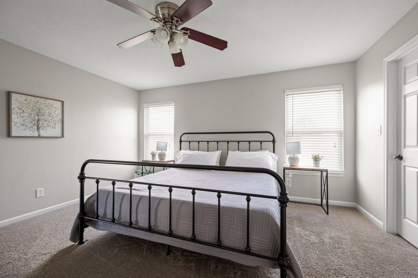 A bedroom with a bed, a ceiling fan, two bedside tables with lamps, and a framed picture on the wall.