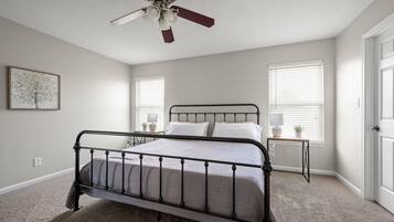 A bedroom with a bed, a ceiling fan, two bedside tables with lamps, and a framed picture on the wall.