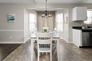 A dining area with a table and chairs, a hanging light fixture, and a kitchen area with cabinets and a dishwasher. - Walk to Ruoff, Pool table, Sleeps 8 (Noblesville)