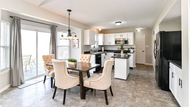 A modern kitchen with white cabinets, a black refrigerator, and a dining area with a table and chairs.
