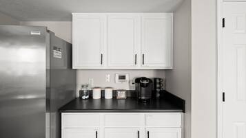 Eine Küche mit weißen Schränken, einem Edelstahl-Kühlschrank, einer Kaffeemaschine und einem kleinen Schild mit der Aufschrift 'HELLO COFFEE'.