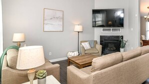 A living room with a sofa, two lamps, a coffee table, a TV, and a fireplace.