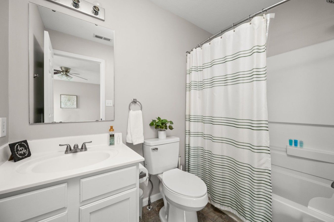 A bathroom with a white sink, mirror, toilet, and striped shower curtain.