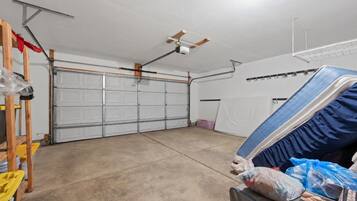 A garage with a ceiling fan, a white garage door, and a workbench with tools and a mattress.