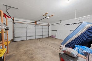 Ett garage med en takfläkt, en vit garageport och en arbetsbänk med verktyg och en madrass.