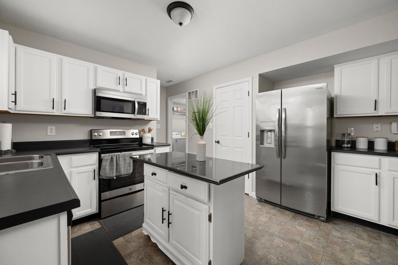 A modern kitchen with white cabinetry, stainless steel appliances, and a black countertop.