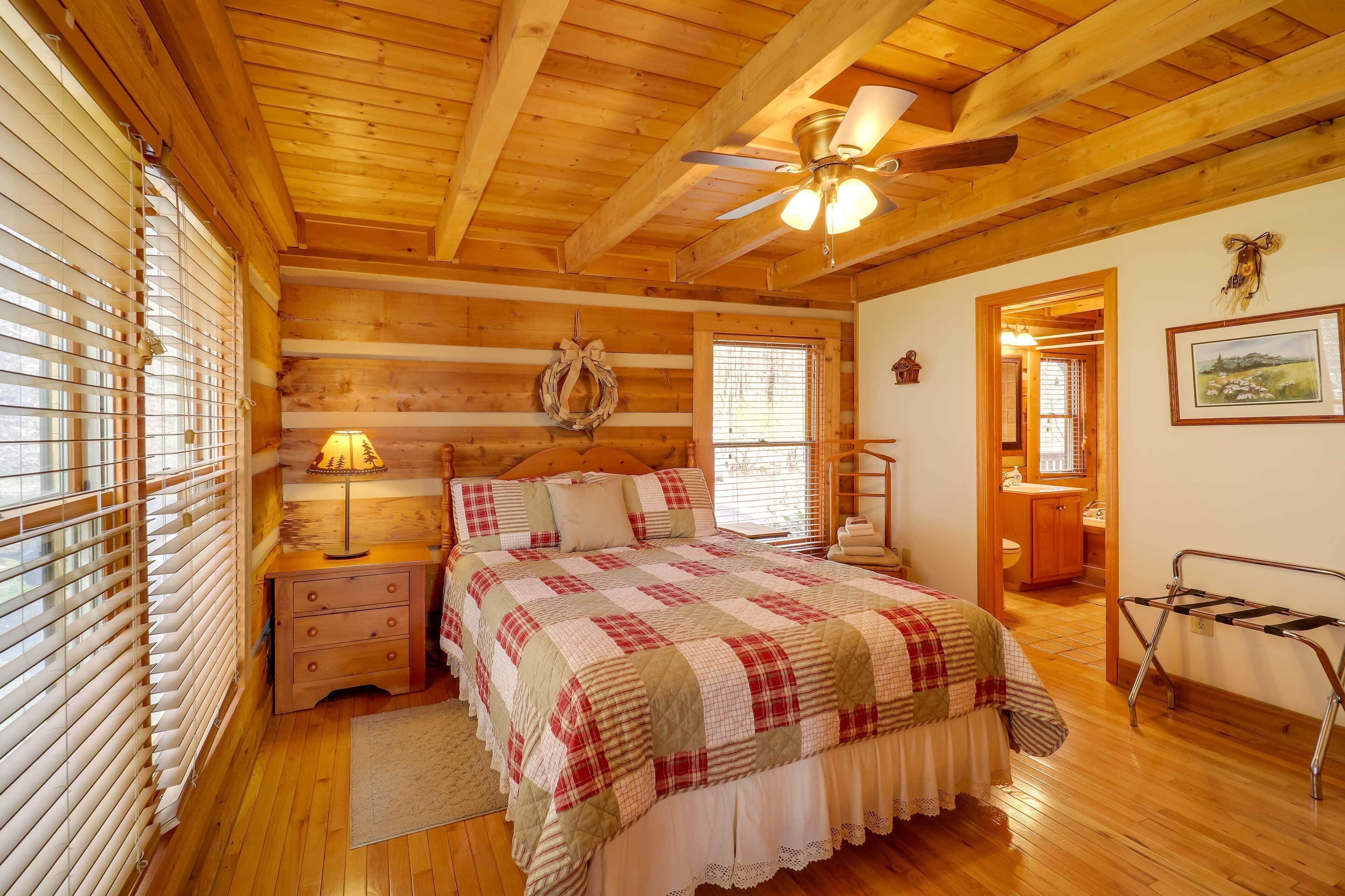 A wooden cabin bedroom with a bed, nightstand, lamp, and a ceiling fan.