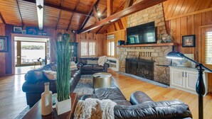 A spacious living room with wooden beams, a stone fireplace, leather sofas, and a large TV.