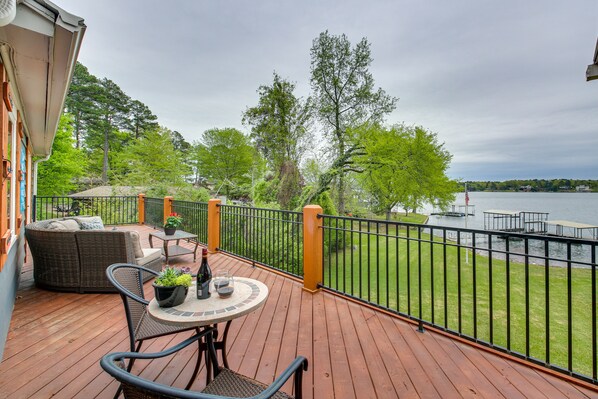 Enjoy waterfront views from this deck with a round table and two chairs, overlooking a dock and a boat.