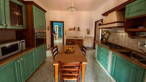 Uma cozinha com armários verdes, uma mesa de jantar, cadeiras, micro-ondas, fogão e um lustre.