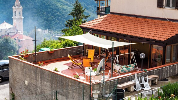 Terraço no telhado com mobiliário externo, antena parabólica e vista para uma montanha e uma igreja.