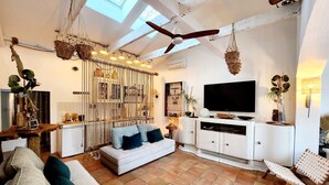 Una sala de estar con sofá, televisor, ventilador de techo y comedor con mesa y sillas.