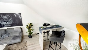 Une pièce moderne comprenant une table à manger, deux chaises, un canapé, une plante en pot et un tableau accroché au mur.