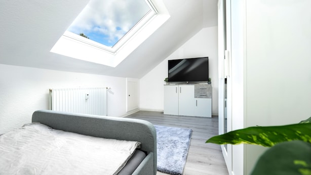 Une chambre moderne avec une lucarne, un lit, un téléviseur en arrière-plan et une petite kitchenette.