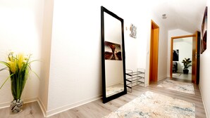 Un couloir avec un grand miroir, un vase avec des plantes, un tableau et une porte en bois.