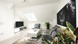 Un salon moderne avec un téléviseur à écran plat, un canapé gris et un grand tableau abstrait.