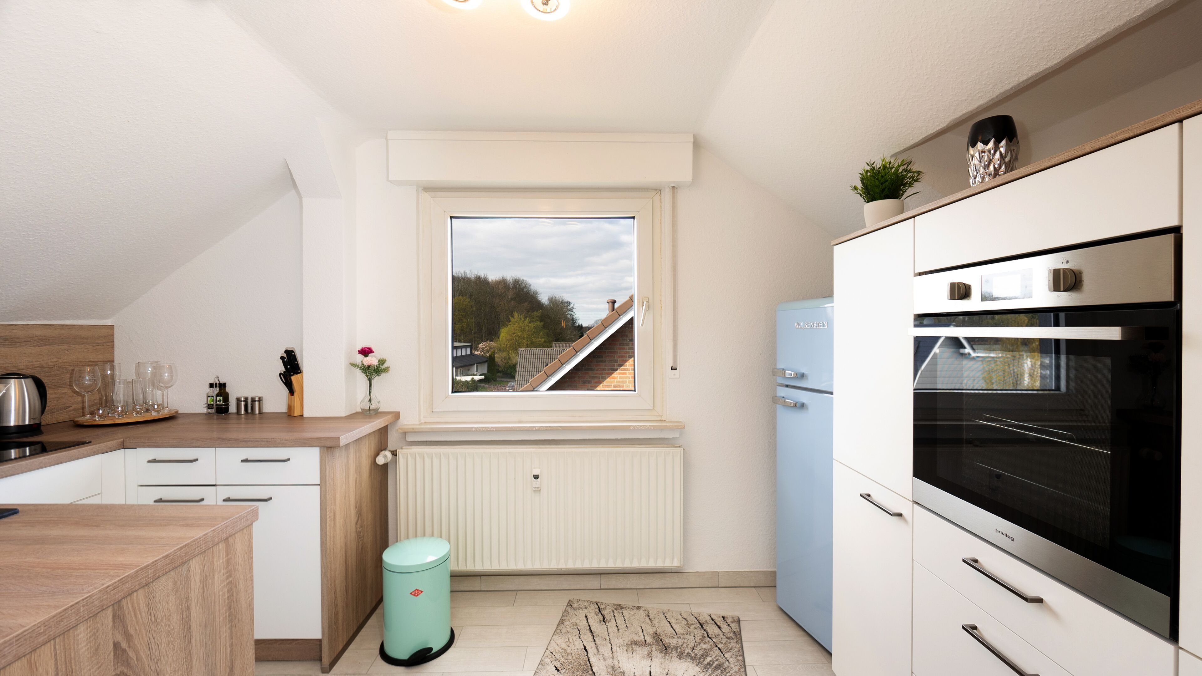 A modern kitchen with a window, white cabinets, a blue refrigerator, and a wooden countertop.