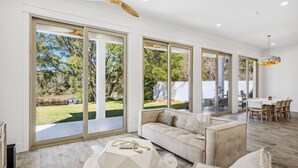 A spacious living room with large sliding glass doors, a wooden ceiling fan, and a dining area with a white table and chairs. - Coastal Lake View & Access! BIGGEST in Rosemary Beach PRIVATE Pool ! Sleeps 18 (Rosemary Beach)
