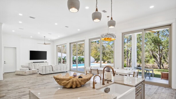 A modern kitchen with a large island, a dining area with a view of the outdoors, and a living room with a flat-screen TV. - Coastal Lake View & Access! BIGGEST in Rosemary Beach PRIVATE Pool ! Sleeps 18 (Rosemary Beach)