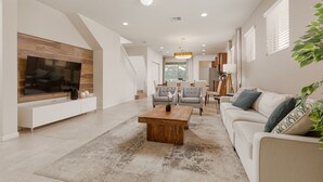 A spacious living room with a large flat-screen TV, a wooden coffee table, and a beige sofa.