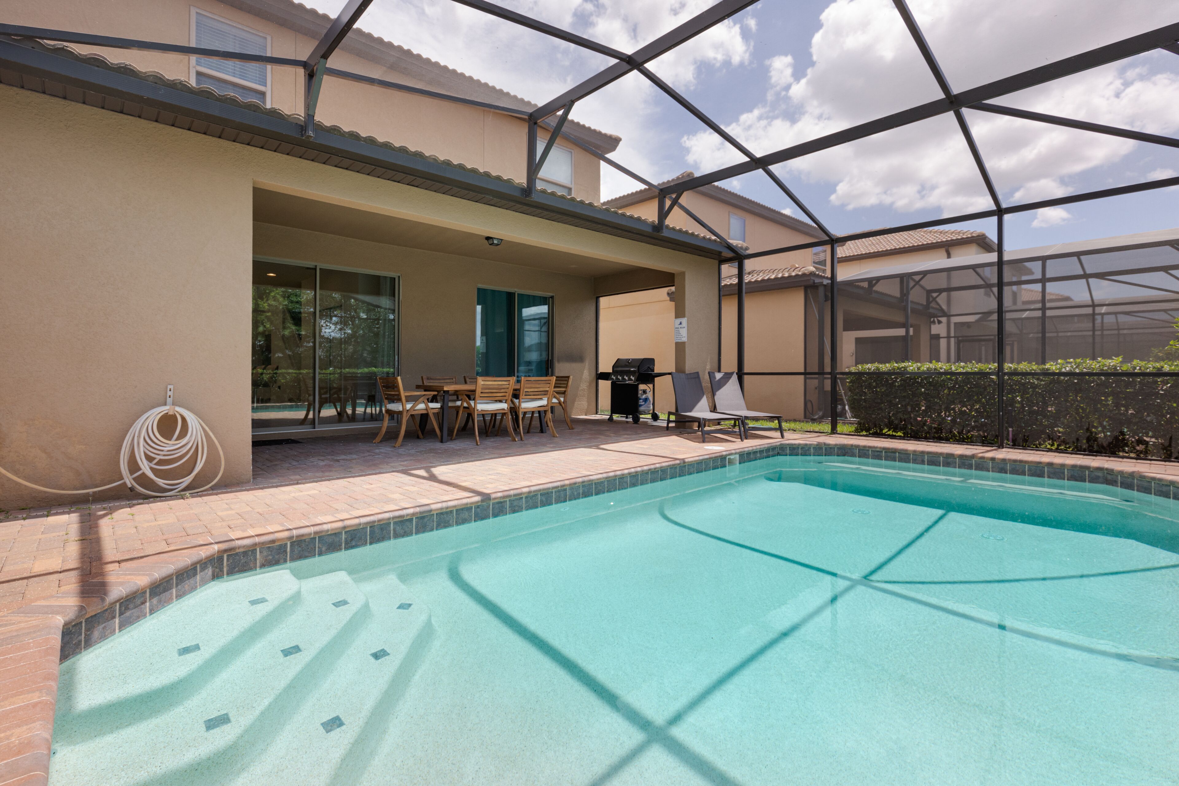 A swimming pool with a covered patio area, outdoor furniture, and a view of the surrounding neighborhood.