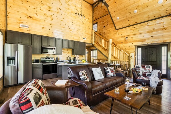 A spacious living area with a brown leather sofa, a wooden dining table, and a kitchen in the background.