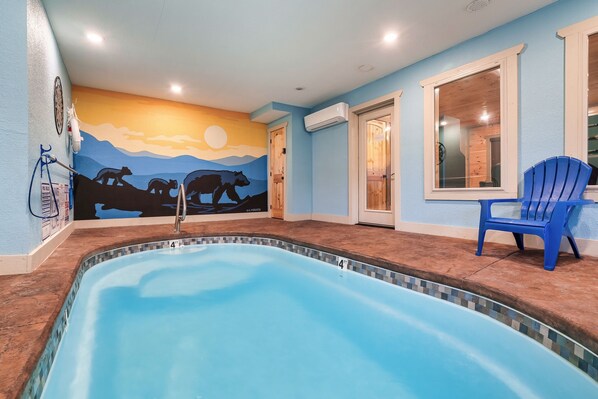 Une piscine ornée d’une fresque murale, une chaise bleue et une porte donnant sur une pièce.