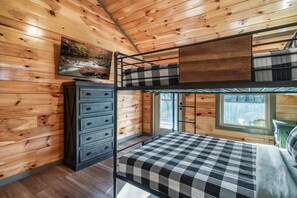 Une chambre avec un lit superposé, des murs en bois, une commode et un tableau représentant une rivière.
