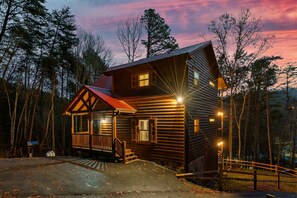 Une cabane en rondins dotée d’une véranda, d’un toit rouge et d’un escalier en bois menant à l’entrée.