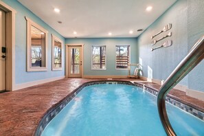 Une piscine intérieure avec un bord carrelé, une rampe métallique et une vue sur l’extérieur grâce à de grandes fenêtres.