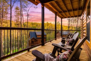 A wooden deck with outdoor seating and a view of a forest. - Luxury Indoor Pool Cabin Near Gatlinburg - Hot Tub, Game Room & Fire Pit (Sevierville)