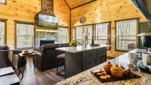A cozy cabin interior with a stone fireplace, wooden ceiling, and large windows. - Luxury Indoor Pool Cabin Near Gatlinburg - Hot Tub, Game Room & Fire Pit (Sevierville)