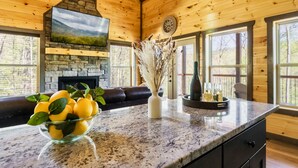 A kitchen with a stone fireplace, a bowl of lemons, and a vase of dried flowers on the counter. - Luxury Indoor Pool Cabin Near Gatlinburg - Hot Tub, Game Room & Fire Pit (Sevierville)