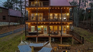 A multi-story log cabin with balconies, outdoor seating, and a fire pit. - Luxury Indoor Pool Cabin Near Gatlinburg - Hot Tub, Game Room & Fire Pit (Sevierville)