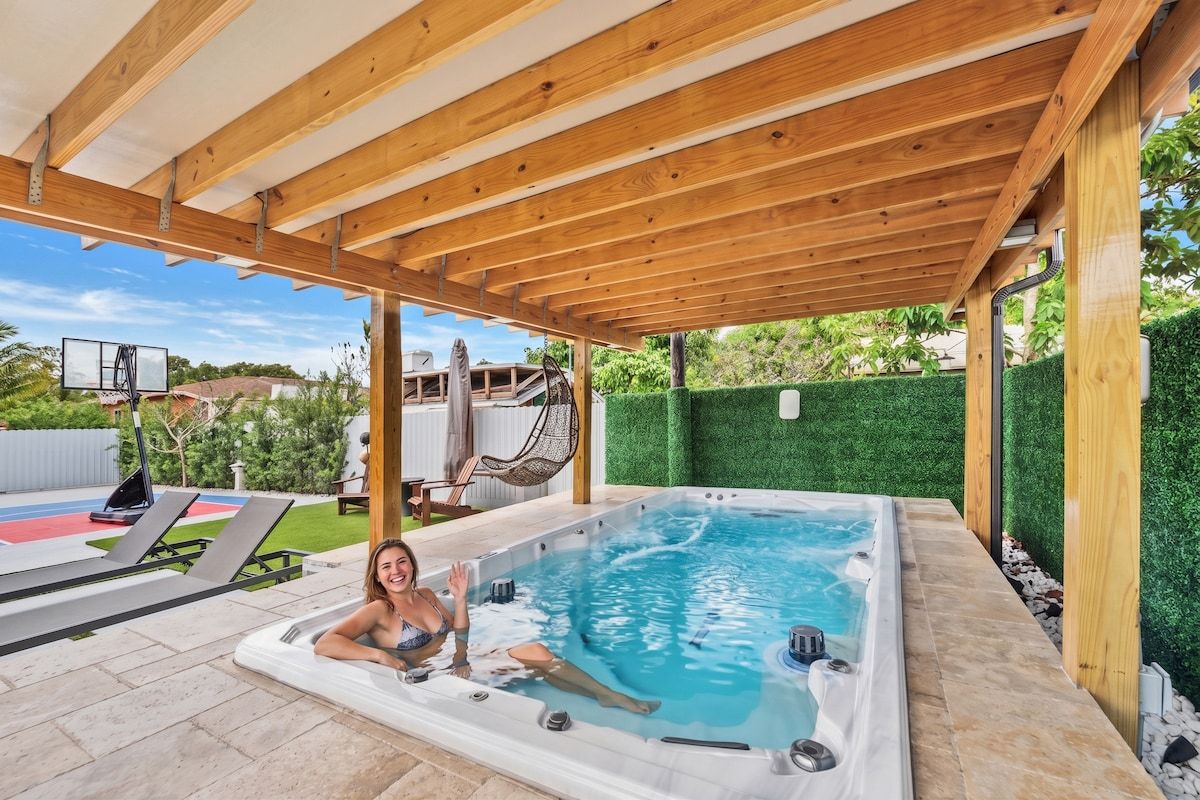 Un jacuzzi bajo una pérgola de madera, con vista a una cancha de tenis y una hamaca.