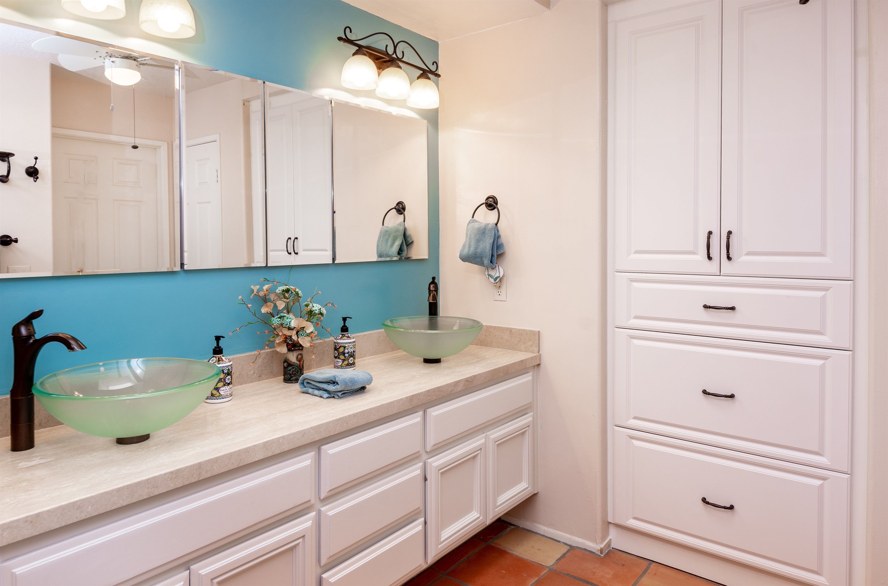 A bathroom with a large mirror, two sinks, a towel rack, and a cabinet.