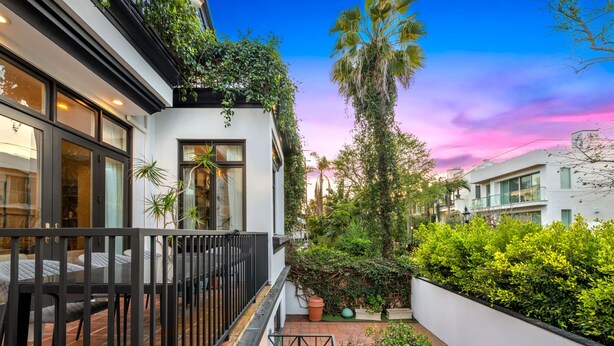 A modern building with large windows, a balcony, and a garden area with various plants and a tall palm tree. - Reef Mall (Marina del Rey)