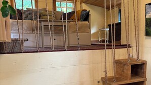 Een rustiek houten interieur met een slaapzolder, houten planken en een hangende schommel.