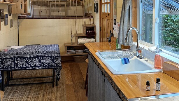 Een gezellig chaletinterieur met een houten plafond, een hangende keukenkast, een eethoek met een bank en een keuken met een spoelbak en fornuis.