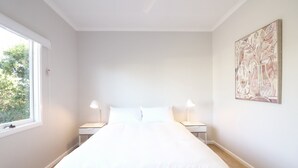 Un dormitorio con una cama grande, dos mesitas de noche, una ventana y una obra de arte en la pared.