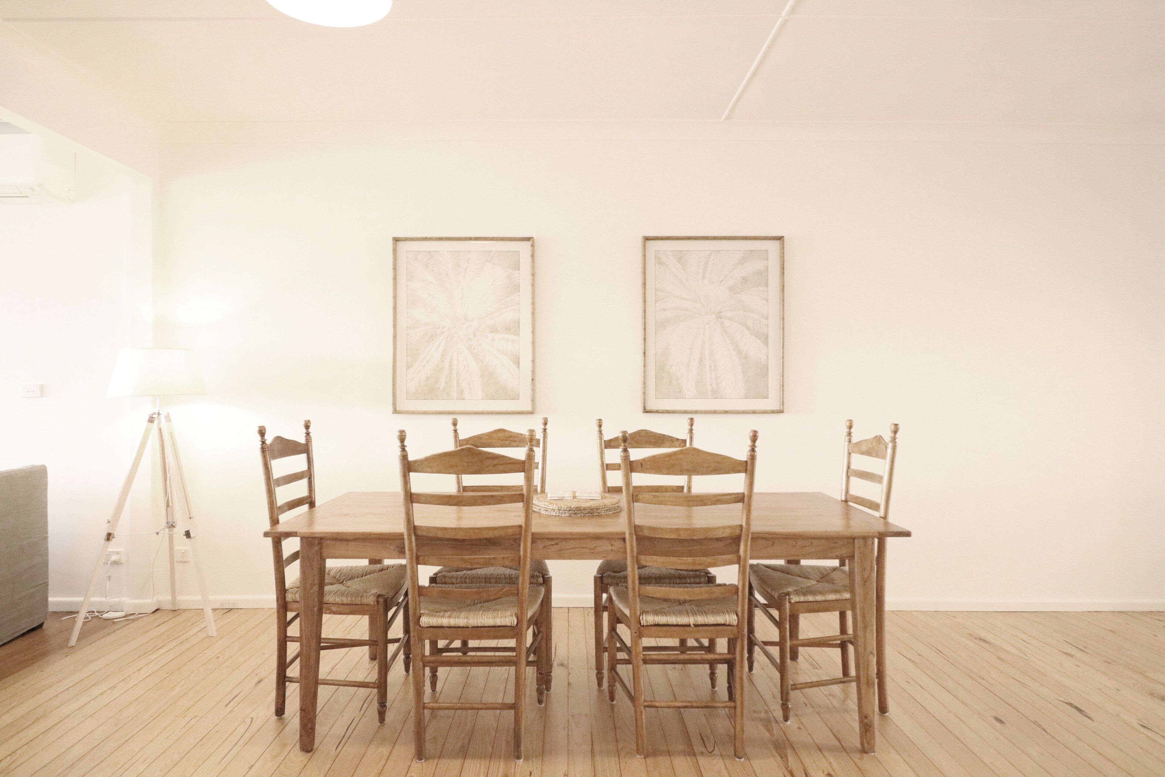 A dining area with a wooden table and chairs, a floor lamp, and two framed artworks on the wall.