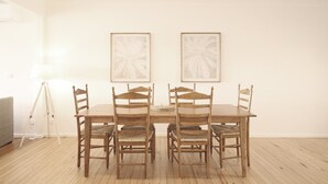 Un comedor con una mesa y sillas de madera, una lámpara de pie y dos obras de arte enmarcadas en la pared.