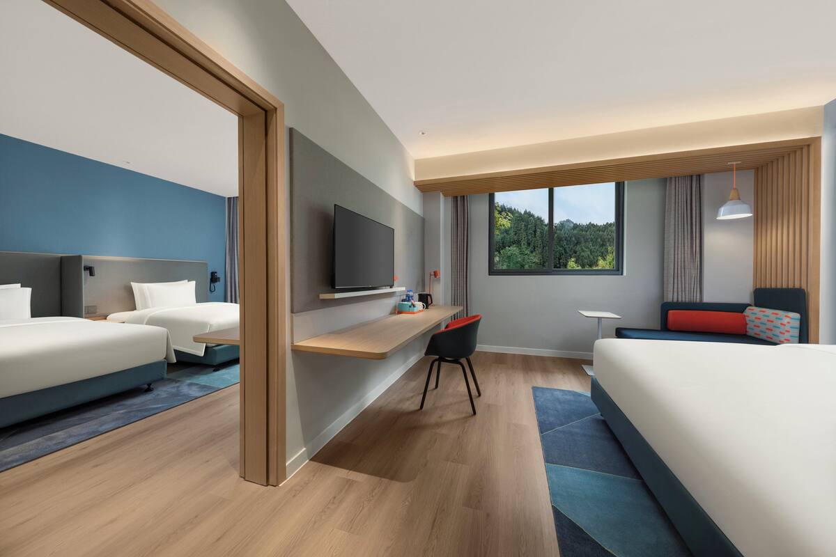 A modern hotel room with a large bed, a desk, a TV, and a view of the outdoors.