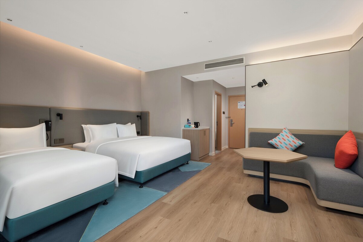 A hotel room with two beds, a sofa, a small table, and a bathroom door.