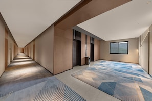 A long, narrow hallway with a patterned carpet, a large window, and a door with a handle. - Holiday Inn Express Wawu Mountain by IHG (Meishan)