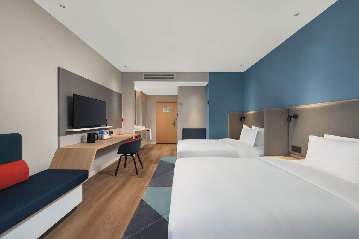 A hotel room with a bed, a desk, a television, and a seating area.