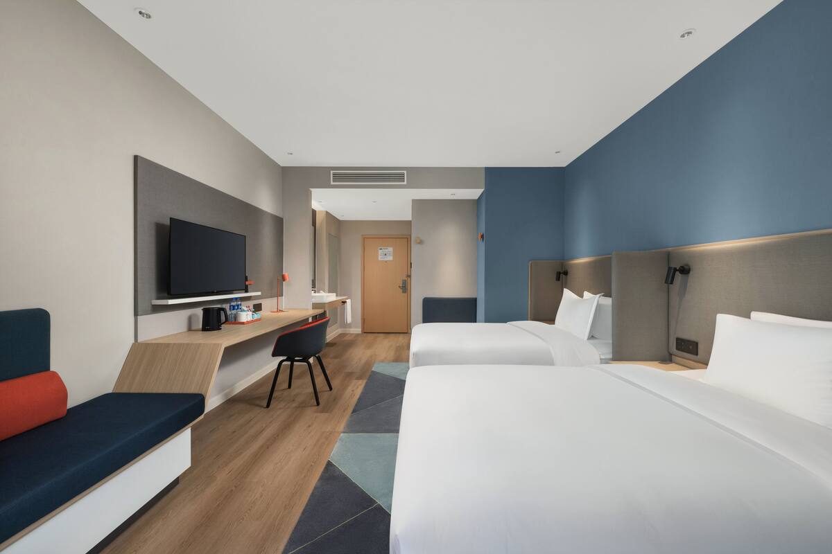 A modern hotel room with a TV, desk, two beds, and a seating area.